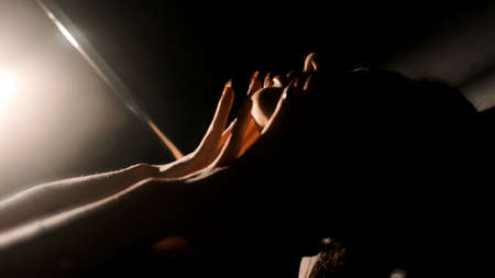 A sexy girl hugs her neck in a backlight with her hands. Black background. Close-up of the handsの写真素材