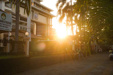 An evening sun that shines bright orange in the evening sunset between trees and urban buildingsのeditorial素材