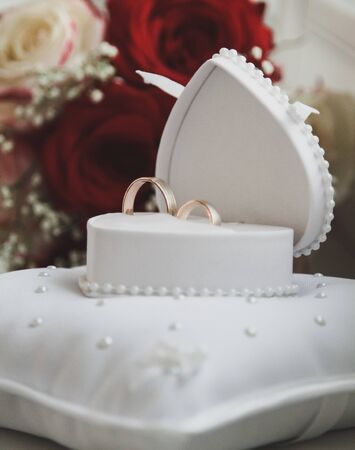 Wedding rings close-up in a white box, in the background a bouquet of brides, roses. The box is like...