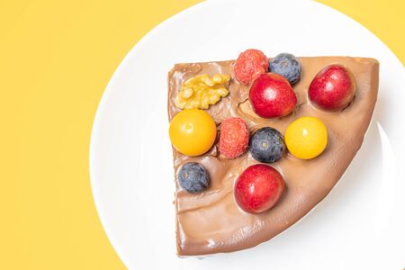 A piece of chocolate berry cake in a white plate on a yellow background. The concept of homemade...
