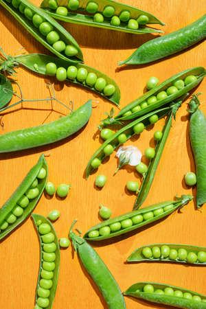 Ripe peas in pods on a yellow wooden background. The concept of summer, pea crop, healthy vitamin food.の写真素材