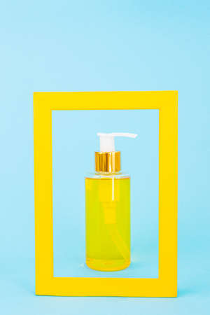 Cosmetic bottle with a dispenser with natural oil is framed by a yellow frame. Blue background. Stylish concept of organic essences, beauty and health products. Minimalism, copy space.の写真素材