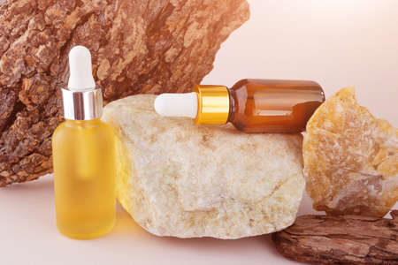 A bottle with a dropper with natural essential oil on a stone, next to a tree bark with a beautiful...