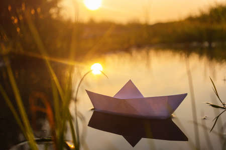 A paper boat floats on the water at dawn. Creative concept of outdoor recreation, river, travel....