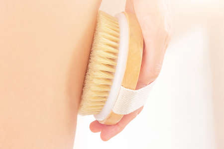 The woman's hand holds a dry brush and massages the top of the leg. The concept of beneficial body...