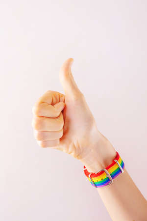 Woman's hand with a raised finger in a bracelet in rainbow LGBT colors. The concept of love, sexual tolerance, LGBT pride, same-sex relationships, homosexuality.の写真素材