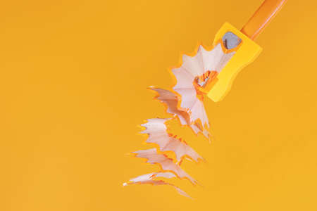 Orange wooden pencil with shavings in a stationery sharpener on an orange background. Monochrome...