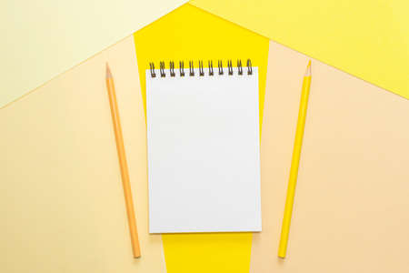 Spiral notebook with blank white sheet and colored pencils on multi-colored paper. The concept of...