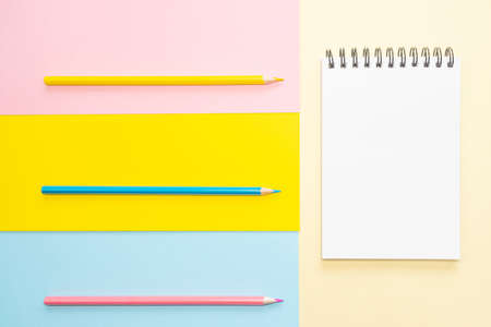 Spiral notebook with blank white sheet and colored pencils on multi-colored paper. Concept of...