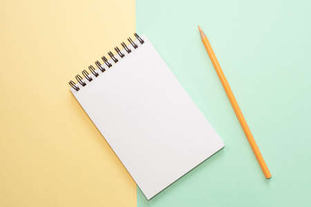 Spiral notebook with blank white sheet and colored pencil on multi-colored paper. The concept of...