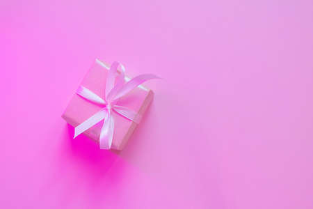 Small square gift in pink wrapping paper with ribbon on pink background, neon lighting. The concept of holiday, presentation, new year, christmas, birthday, celebration. Copspace, flat lay, minimalismの写真素材