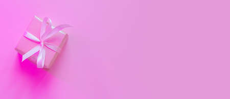 Small square gift in pink wrapping paper with ribbon on pink background, neon lighting. The concept of holiday, presentation, new year, christmas, birthday, celebration. Copspace, flat lay, minimalismの写真素材