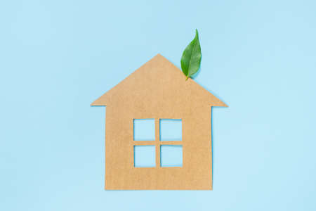 House made of craft paper and green leaves of a plant on a light blue background. Eco-friendly home concept, healthy lifestyle, zero waste.の写真素材