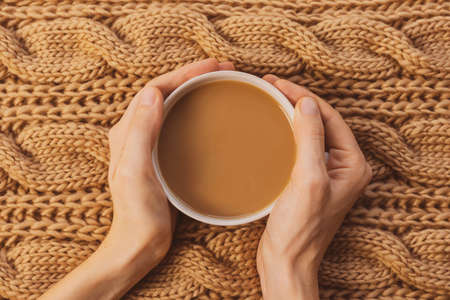 Cozy home still life: white cup with coffee, female hands, chunky knit scarf. Winter concept. Warm shades, close-up.の写真素材