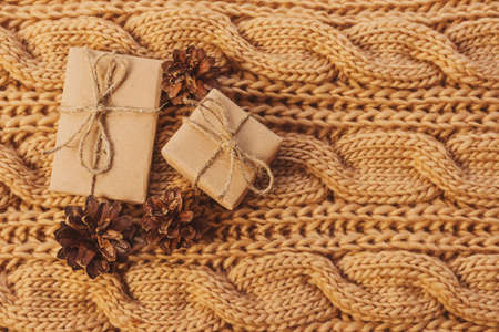 Cozy home still life: large-knit scarf, gifts in craft paper, pine cones. Concept for winter coming, christmas eve, new year, hygge. Warm shades, close-up.の写真素材