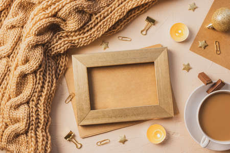 Cozy home flat lay: white cup with coffee, golden photo frame with empty space inside, chunky knit scarf, gift. The concept of the coming winter, christmas eve and new year. Warm shades, close-up.の写真素材