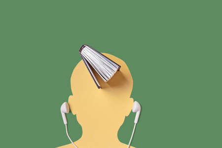 A silhouette of a man's head, next to a headset, and a book on top. Audiobooks, lectures, podcasts, teaching concept. Minimalism, copy space.の写真素材