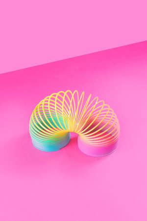 Toy plastic rainbow on a pastel pink background. A colored spiral for play and stunts, popular in the 90s. Minimalism. The concept of toys, childhood. brightness.の写真素材