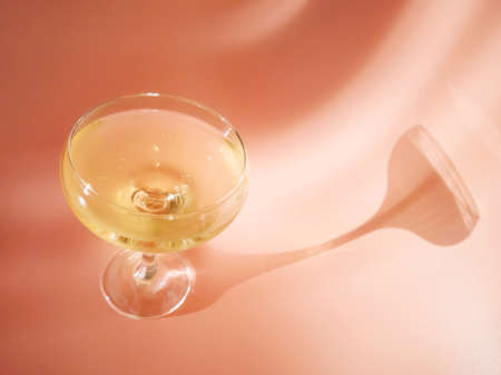 A glass of champagne on a pastel pink background. Bright sunlight, a spectacular long shadow comes from the glass. Creative concept of holiday, celebration, party, alcohol.の写真素材