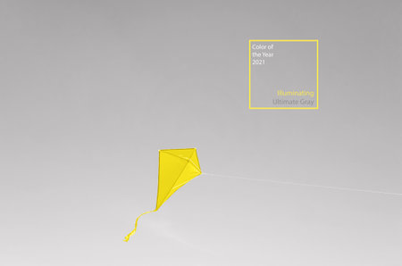 A yellow kite soars in a cloudless gray sky. Illuminating and Ultimate Gray. Colors of the year 2021. The trendy concept of freedom, summer hobbies, entertainment in nature. Minimalism, copy space.の写真素材