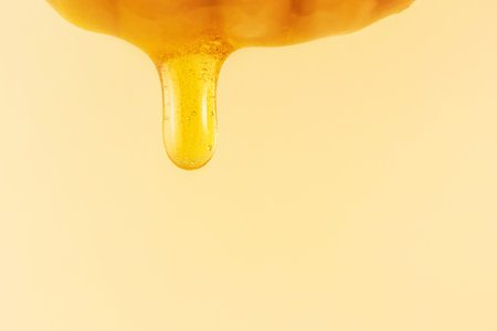A drop of honey flows down from a wooden spoon. Macro photography, copy space.の写真素材