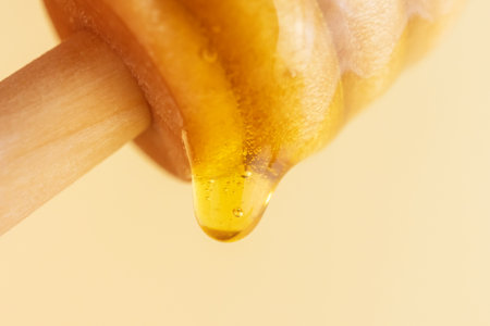 A drop of honey flows down from a wooden spoon. Macro photography, copy space.の写真素材