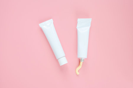 White cosmetic tubes on a pink background. Concept of face and body skin care, cosmetics. Top view,...