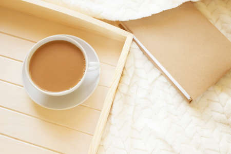 Wooden tray with a cup of coffee on a light blanket. There is a book nearby. View from above. The concept of a morning, weekend, relaxing home.の写真素材