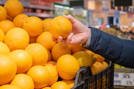A man's hand takes a ripe orange from a box with oranges in a supermarket. The concept of choosing and buying products in a store, sales.の写真素材