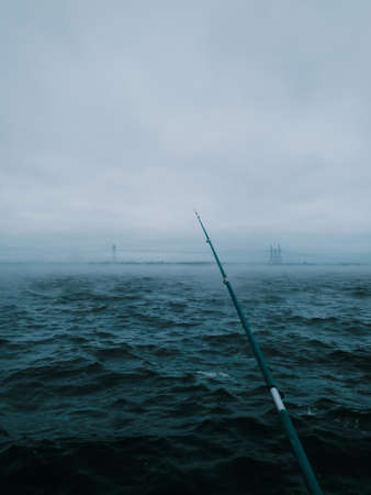 Fishing concept: spinning rod thrown into the river. Cloudy weather, evening. Vertical photography, copy space.の写真素材