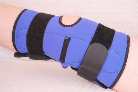 Blue bandage on the knee joint, orthosis on the knee joint after injury or surgery. Close-up, male knee, athleteの写真素材