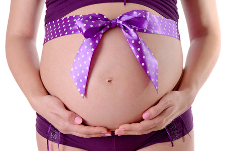 close up of pregnant belly wth decorated with violet dotty ribbon isolated on white background