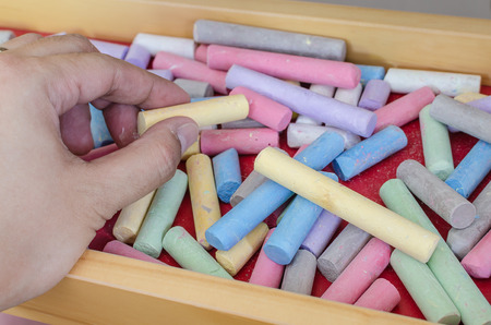close up to hand holding chalk with multicoloured chalk in trayの写真素材