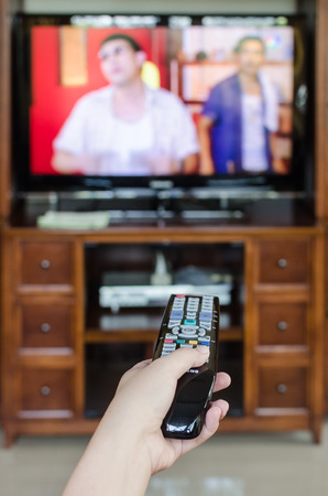 Hand holding TV remote control with  television in the backgroundの写真素材
