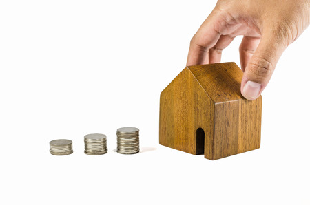 hand try to pick up wooden toy house with coins concept of dearness of habitation on white backgroundの写真素材