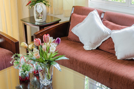 living room with pillows on red wooden sofa and vase of flower on tableの写真素材