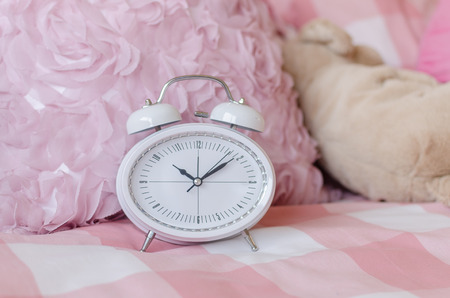 white modern alarm clock on pink bed in bedroomの写真素材