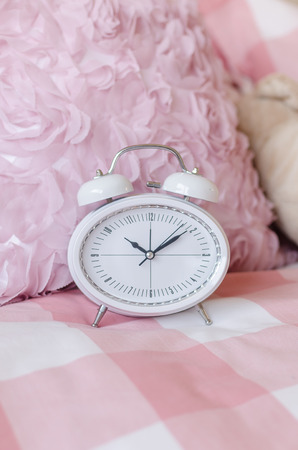 white modern alarm clock on pink bed in bedroomの写真素材
