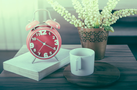 retro photo style of modern red alarm clock on book with cup on wood tray and plant in vaseの写真素材