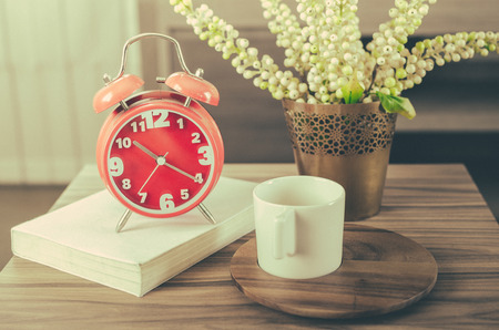 vintage photo style of modern red alarm clock on book with cup on wood tray and plant in vaseの写真素材