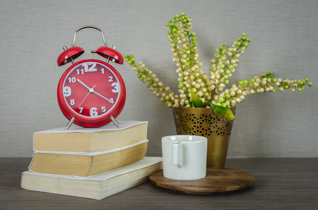 modern red alarm clock on book with cup on wood tray and plant in vaseの写真素材