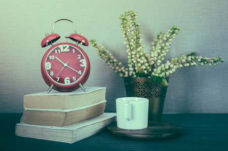 retro photo style of modern red alarm clock on book with cup on wood tray and plant in vaseの写真素材