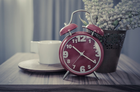 retro photo style of red alarm clock on table with cup on tray and plantの写真素材