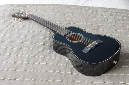 black acoustic guitar on bed in bedroomの写真素材
