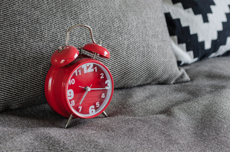 red alarm clock on bed with grey pillows