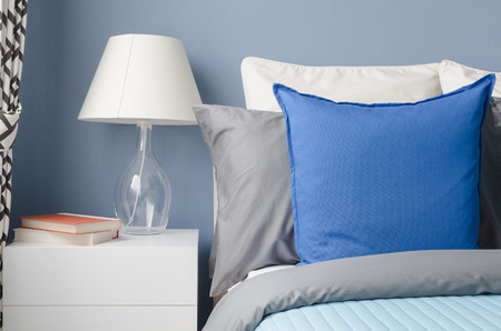 blue pillow on bed with glass lamp on white table in modern blue bedroom at homeの写真素材