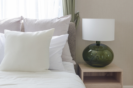white pillows on bed with modern white lamp on wooden table side in modern bedroomの写真素材