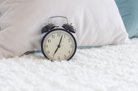 modern black alarm clock on bed with white blanketの写真素材