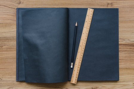 blank black notebook with black pencil and ruler on wooden desk