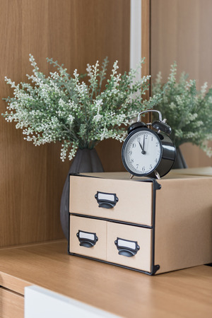 white alarm clock with brown box and plant on wooden dressing tableの写真素材